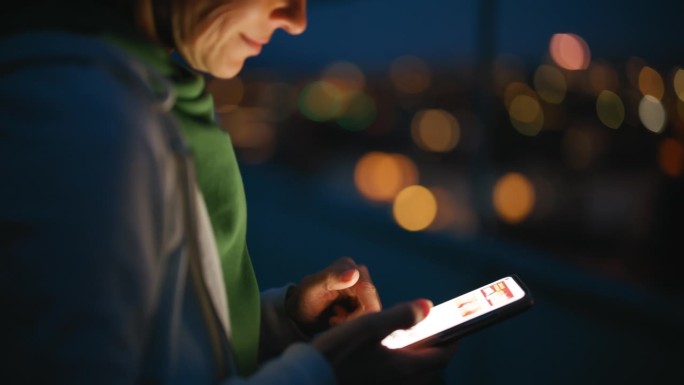 夜间在城市屋顶上使用智能手机的女子特写