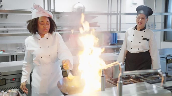 厨师学生在带煤气灶的厨房里用炒锅学习炒菜课，高级厨师老师微笑着与厨师学生在烹饪课上的成就合影