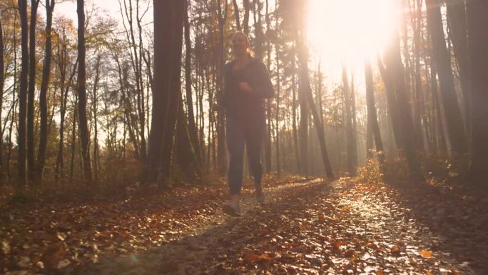 肖像，镜头光晕:快乐的跑步者在美丽的秋林中慢跑