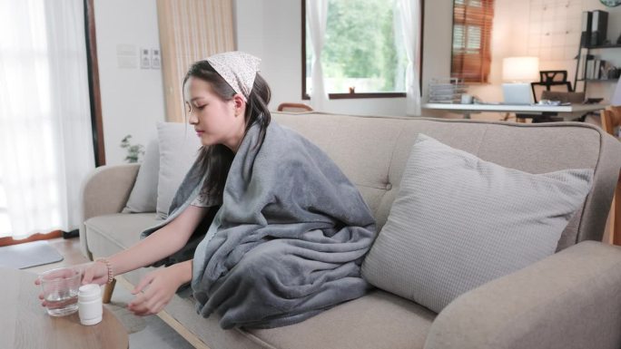一个十几岁的女孩在吃药的时候发烧了，在毯子里瑟瑟发抖。
