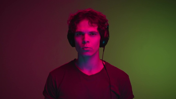 在室内拍摄的霓虹灯下，戴着耳机听音乐的年轻人的肖像。一个酷的家伙听到网络Mp3播放器的在线歌曲。千禧