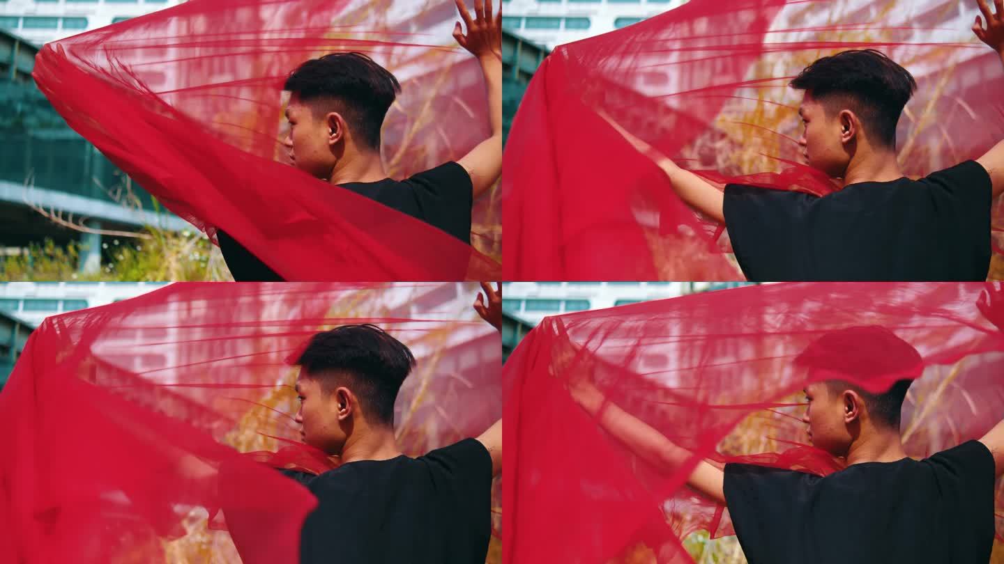 一名亚洲男子双手拿着一条红领巾，风一吹，巾就被吹走了
