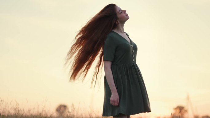 有一头红长发的女孩在夕阳下的田野里翩翩起舞。