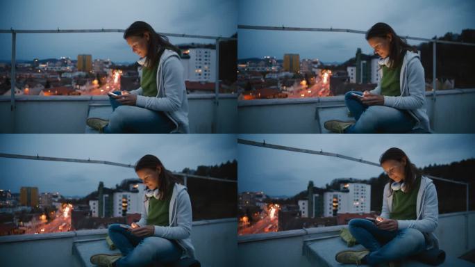 深褐色头发的女人晚上坐在城市屋顶上使用智能手机