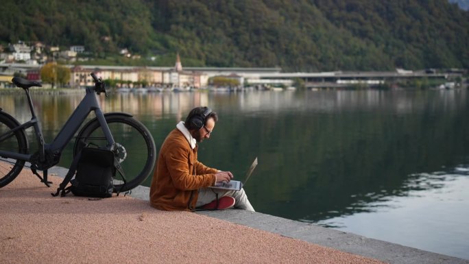 工作与自然相遇:一个人在湖边的木板路上骑着电动自行车和笔记本电脑
