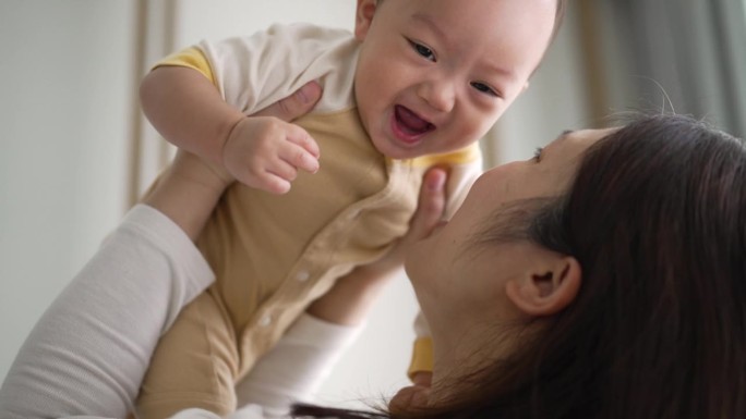 幸福的母子在家里亲吻并将男婴抛向空中