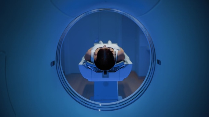 在医学实验室，躺在CT或MRI扫描床上的匿名女性患者在专业放射科医生的监督下接受扫描程序。床向相机移