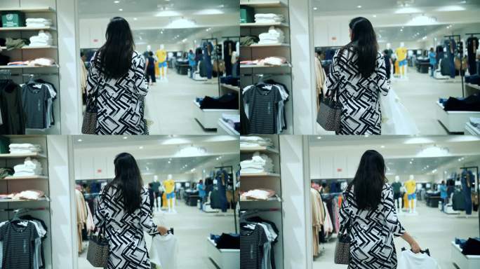 购物。购买。一个年轻的女人走过一家服装店，环顾四周，检查挂在衣架上的东西。后面的观点。购物中心。摩尔