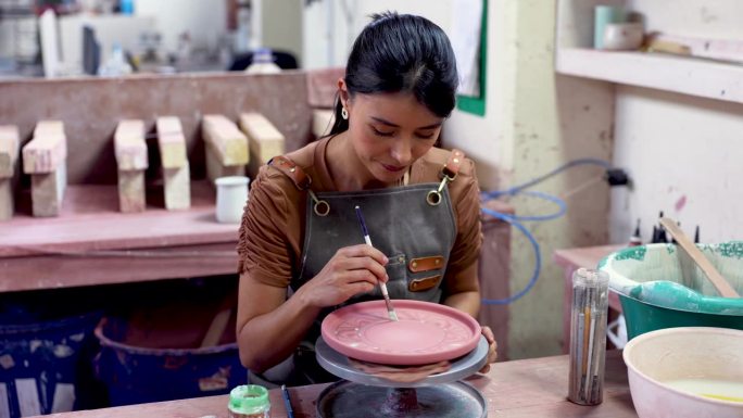 在陶瓷厂，一名拉丁美洲妇女正在用小轮子绘制陶瓷盘