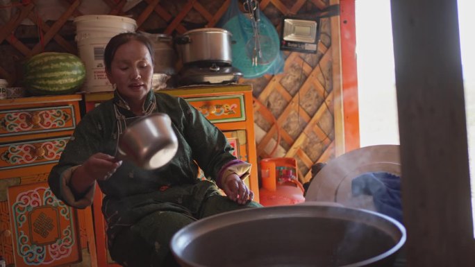 蒙古游牧妇女在蒙古包里为客人准备传统的奶茶，倒进杯子里