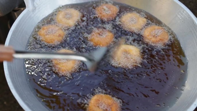 高角度的食物摊贩在本地市场用大量热油在大锅中烹煮圆形油炸虾饼或泰式托德门宫。泰国街头小吃。油炸食品。