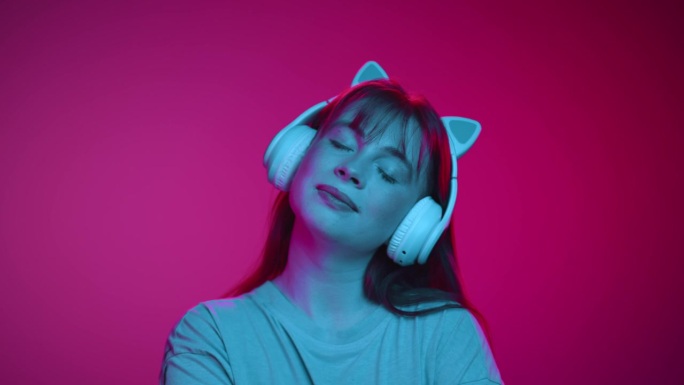 在室内拍摄的霓虹灯下，戴着耳机听音乐的快乐女人的肖像。一个平静的女孩听到网上Mp3播放器的声音。在可