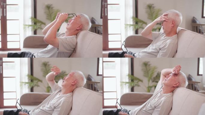 亚洲老年男性坐在家里的沙发上头痛，工作压力大，痛苦和悲伤，无法入睡