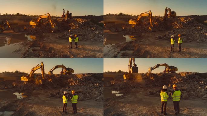 空中无人机拍摄的建筑工地在阳光明媚的晚上:工业挖掘机挖掘岩石，并把它们装上卡车。土木工程师和检查员观