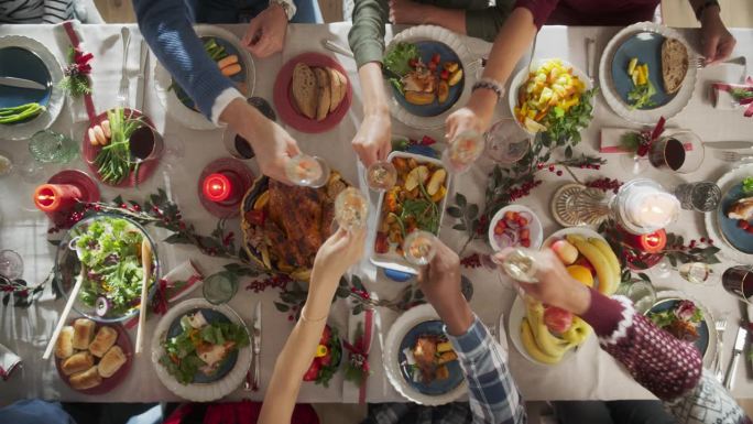 家人和朋友聚在家里吃传统的圣诞晚餐，烤火鸡盛宴。从上往下看，人们举起香槟酒杯举杯，一起庆祝节日