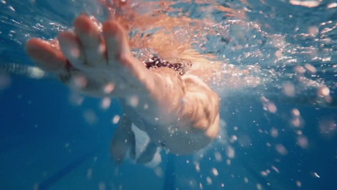 水下镜头:健美肌肉的游泳者在游泳池里做圈。英俊的职业运动员以极快的速度游泳-准备创造世界冠军纪录。时