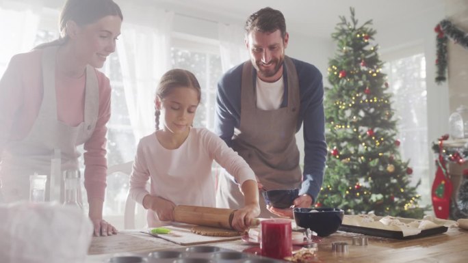 家庭庆祝节日:父母和孩子在圣诞节期间一起烘焙的慢动作手持镜头。可爱的小女孩和父母做姜饼饼干。童年快乐