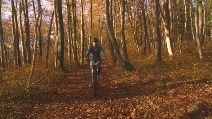 肖像:秋天，微笑的女子骑着电动自行车穿过色彩斑斓的森林