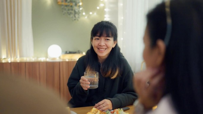 一名年轻女子在家里的晚宴上和朋友们一起喝水聊天。