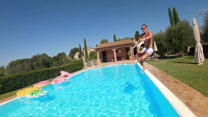 水下镜头:运动员在游泳池里跳跃，造成很多泡沫。一个男人在炎热的夏日享受茶水，在温泉或酒店游泳的跟踪镜