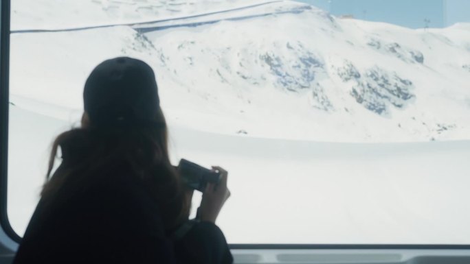 一名亚洲女游客在瑞士雪山上的火车上拍摄度假照片。