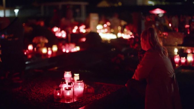 在亡灵节的夜晚，女人坐在灯火通明的墓地旁