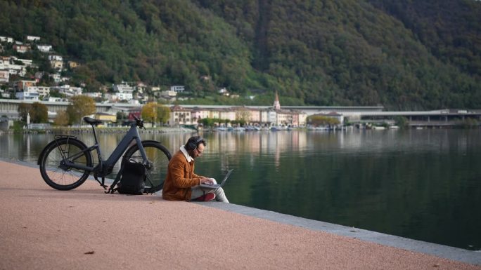 工作与自然相遇:一个人在湖边的木板路上骑着电动自行车和笔记本电脑