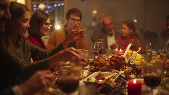 快乐的家庭成员享受节日大餐，在餐桌上分享食物，在圣诞火鸡晚餐期间进行有趣的交谈和快乐。家充满节日气氛