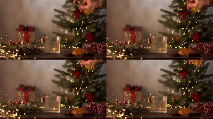 酒保调制圣诞鸡尾酒。在玻璃上洒上金色的喷雾。背景里有花环和礼物的圣诞树。切成片的橘子，肉桂，八角，红