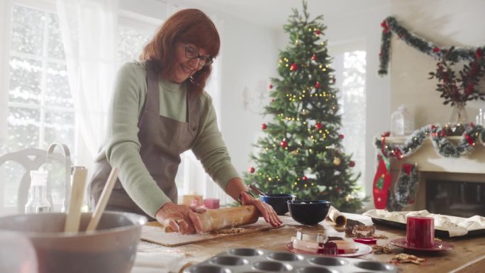 老年妇女在家里为圣诞节制作姜饼饼干的慢动作肖像。奶奶快乐地做糕点与家人和朋友分享，准备节日聚会和晚餐