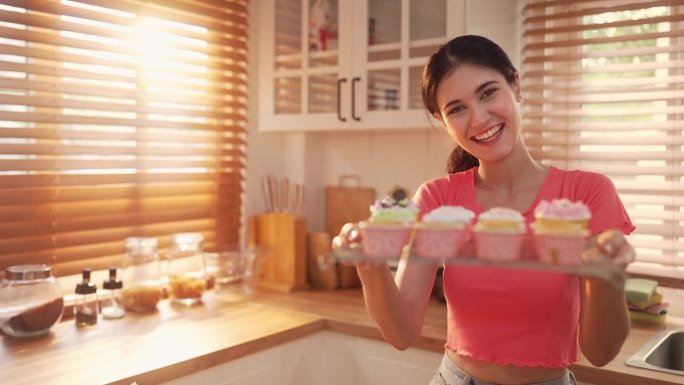 女人在厨房里微笑着展示新鲜的纸杯蛋糕，慢镜头