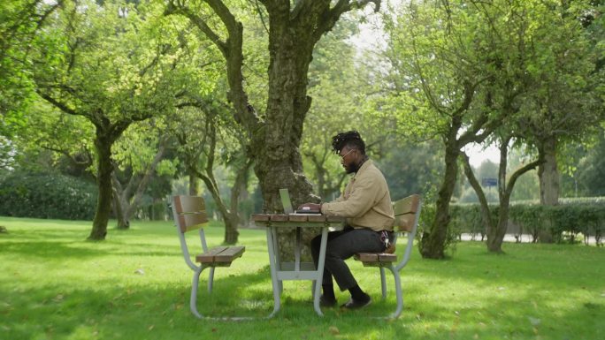 一个人在公园的野餐桌旁工作，用他的笔记本电脑打字