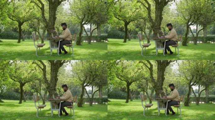 一个人在公园的野餐桌旁工作，用他的笔记本电脑打字