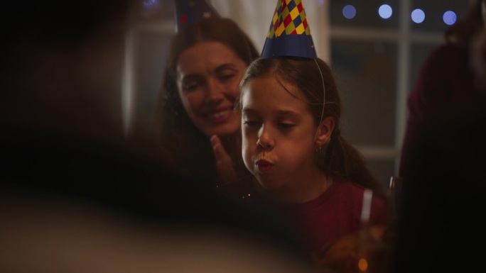 一家人和一个小女孩一起庆祝生日。爸爸拿着庆祝蛋糕，小女儿吹着蜡烛，许下快乐的愿望。快乐的孩子被她的近
