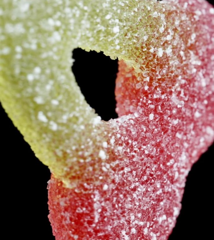 樱桃糖树枝上樱桃形状的有嚼劲的软糖，上面撒上糖在一个特写镜头中，它在黑色的背景上旋转，孤立的。