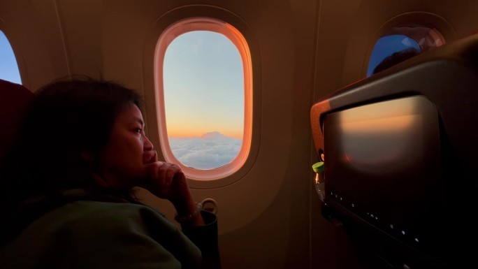 一名女子坐在飞机上，在日落时分看着窗外
