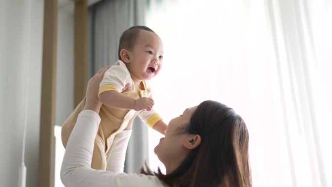 幸福的母子在家里亲吻并将男婴抛向空中