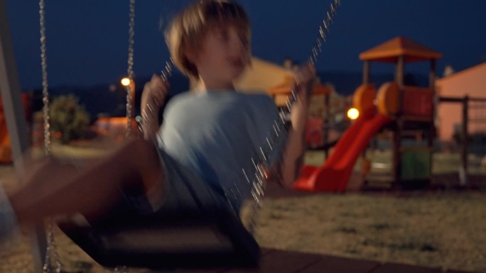 夜间，一个孩子在操场上玩秋千
