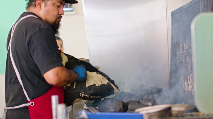 男厨师在墨西哥餐厅里把煤卸到烤架上