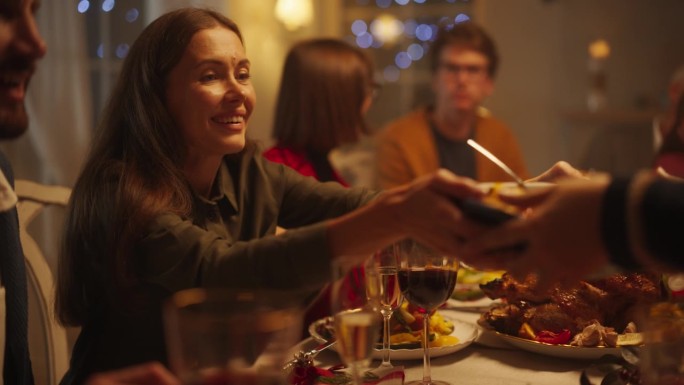 一个女人和家人在一张大桌子旁吃饭的肖像。亲人谈笑风生，享受美食。亲密的晚餐设置与不同的客人庆祝圣诞节