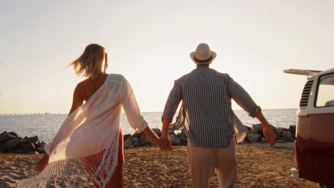 跟踪的男人和女人在爱跑在沙滩上与小型货车公路旅行。新婚夫妇在美丽的小岛上度蜜月，享受夏日的慢动作