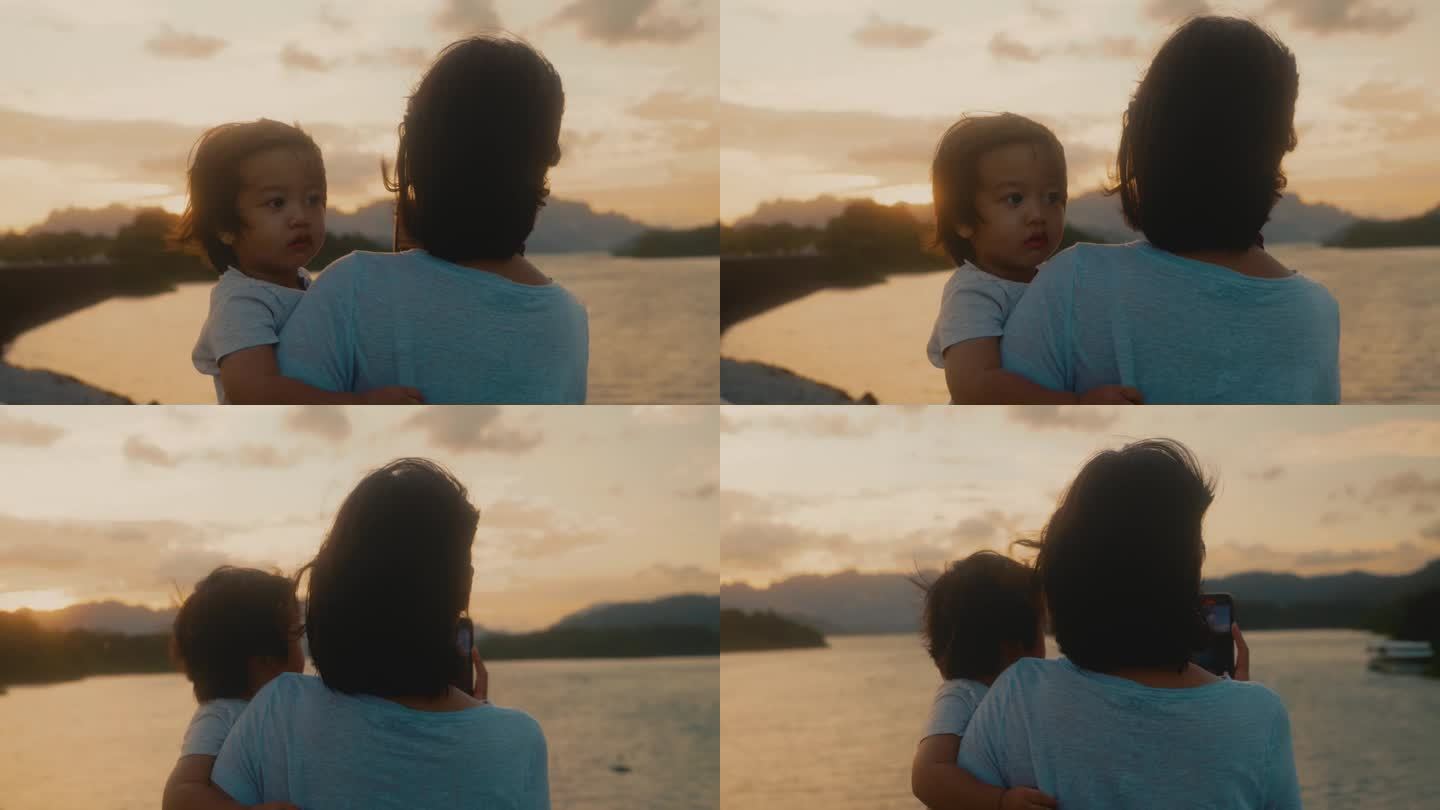 亚洲母亲抱着儿子在拉查帕哈大坝看日落。素叻他尼。