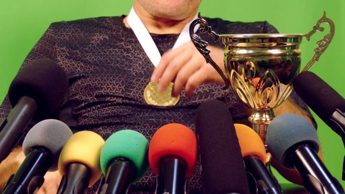 特写:运动员拿着奖杯和奖牌站在绿色背景的媒体麦克风前
