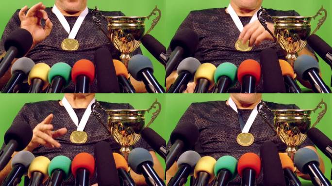 特写:运动员拿着奖杯和奖牌站在绿色背景的媒体麦克风前