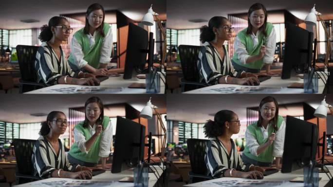 黑人女性游戏设计师使用带有动画软件的台式电脑，并在游戏开发工作室办公室与亚洲女性项目经理交谈。不同的