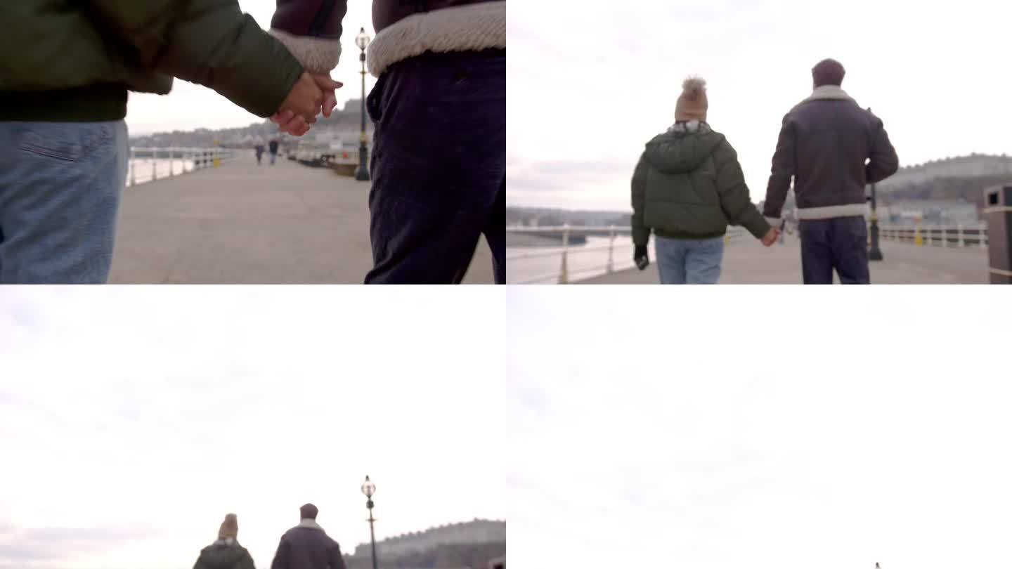 在海边牵手从镜头前走过情侣夫妻河边走路散