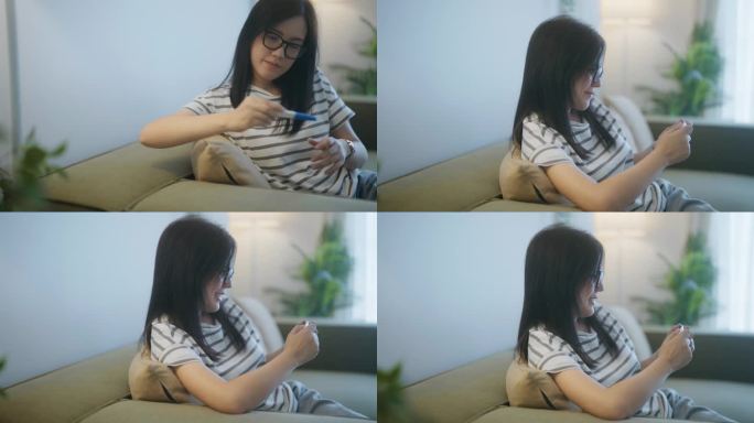 一位年轻的亚洲女性坐在家里客厅的沙发上，手里拿着验孕棒呈阳性的结果，面带微笑。