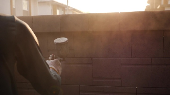 图为，亚洲地区的建筑工人正在用喷枪粉刷房屋外墙。