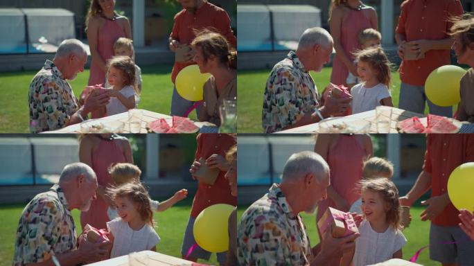 快乐的小女孩在夏季花园的一代家庭生日聚会上给她的老祖父送生日礼物。