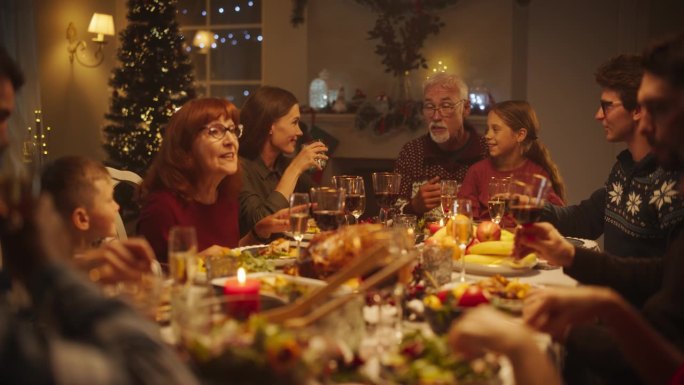 爷爷给年幼的孙女讲有趣的童年故事，孙女和来自不同文化背景的家人朋友坐在圣诞餐桌上。晚上的节日晚宴